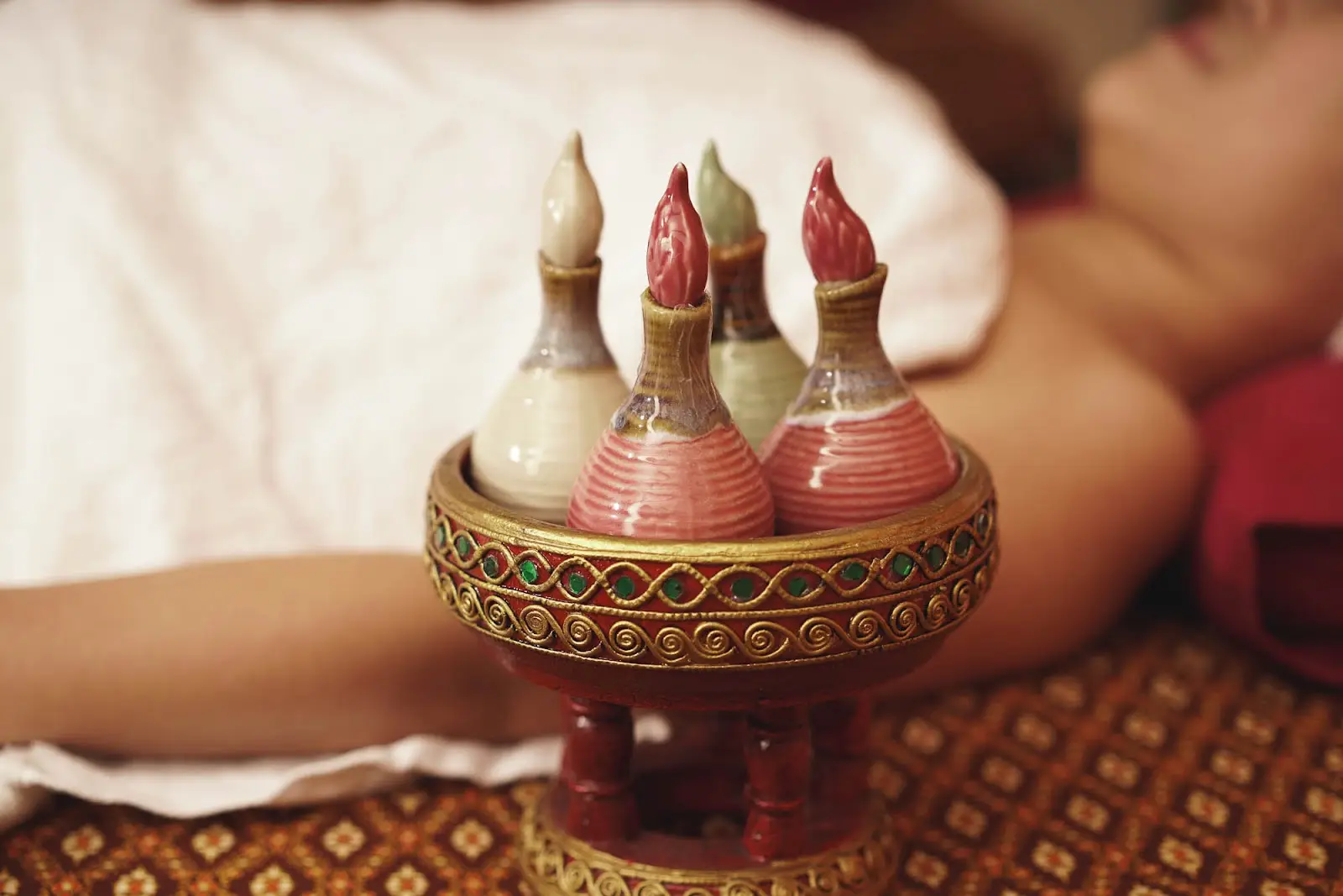 Traditional herbal oil bottles on a carved tray beside a massage bed